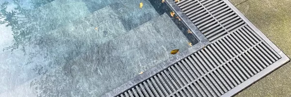 Deck drain channel set between pool deck pavers directing rainwater away