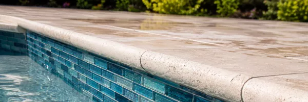 Close-up of new glass waterline tile and stone coping on pool edge