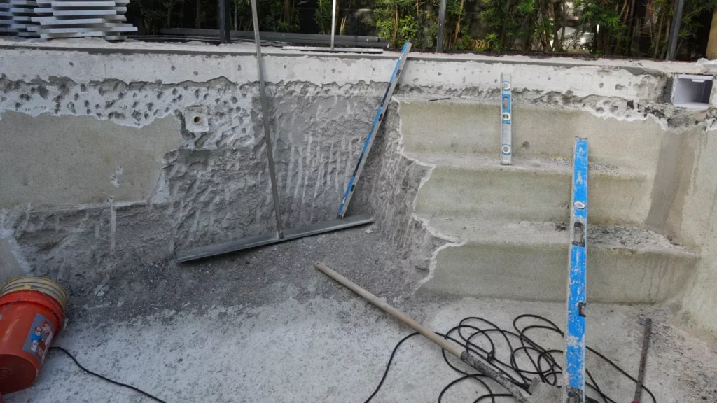 Worker chipping old plaster from pool shell wall